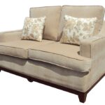 Beige upholstered Malia 2-Seater Sofa with floral patterned throw pillows and wooden base.